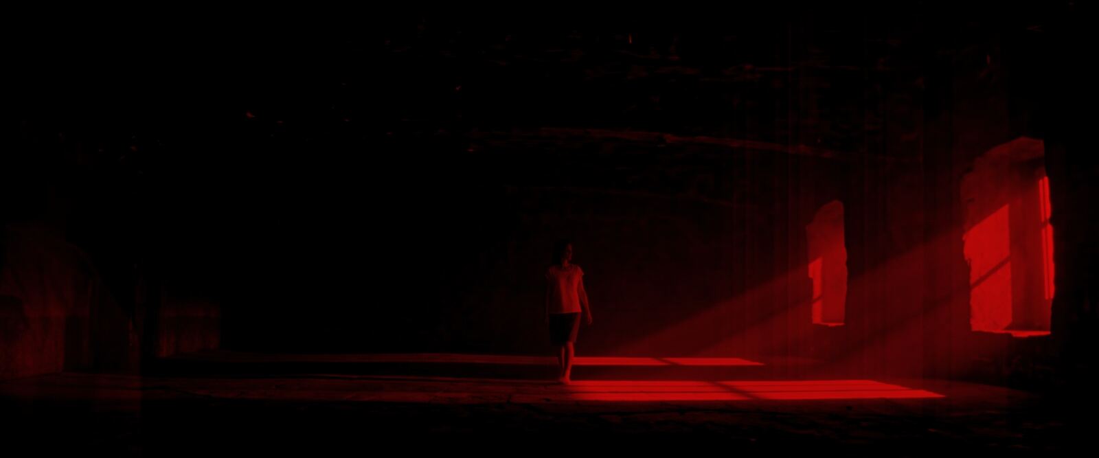 The room drenched in deep red, the figure small in a shaft of light from two windows.