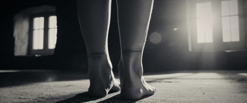 Close low-angle of bare feet and ankles standing on a dusty concrete floor.