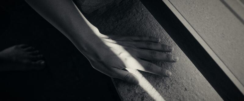A hand rests flat on a rough concrete sill split by a hard edge of light.