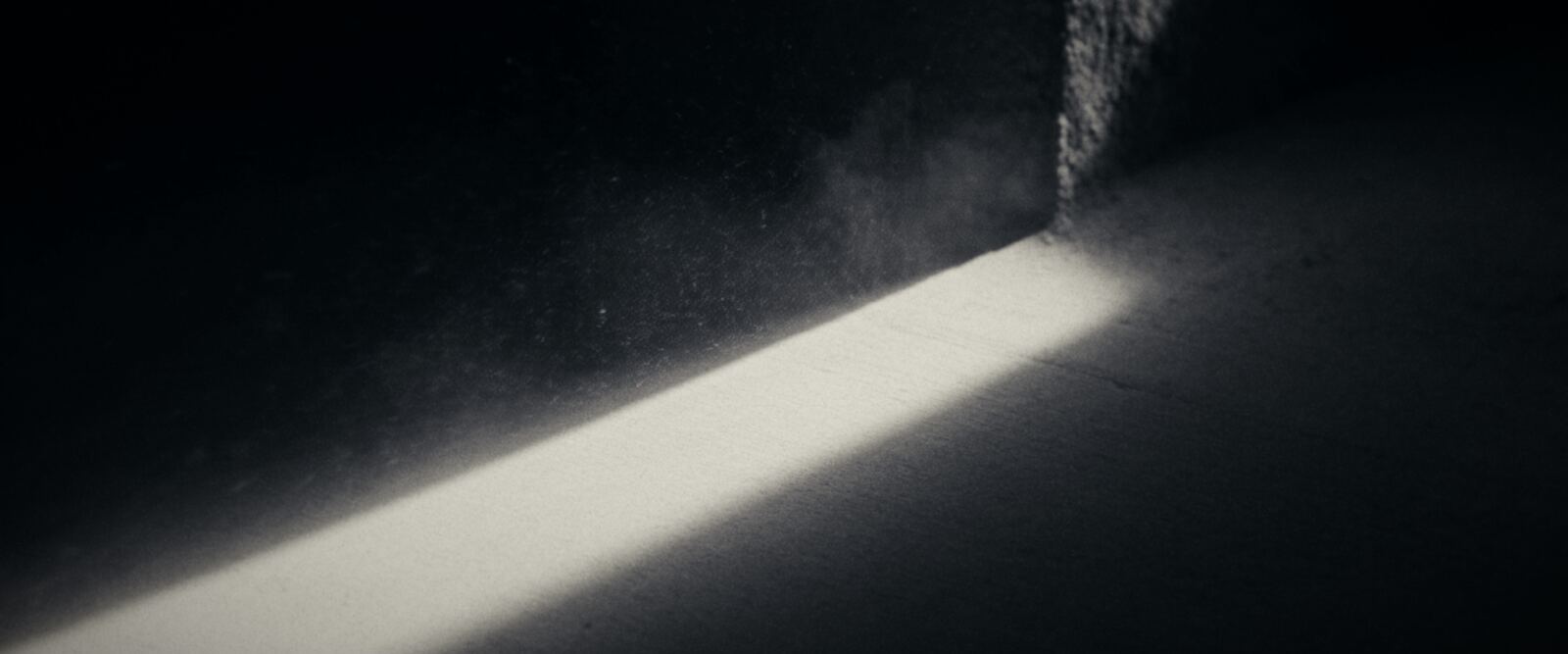 A hard bar of daybreak light cuts across a concrete floor, dust suspended in the beam.