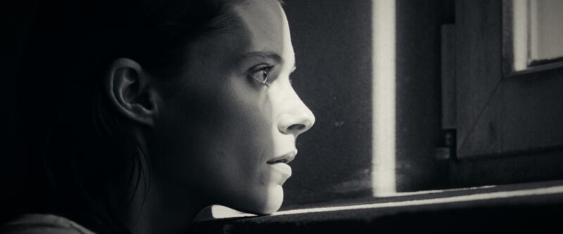 Profile of a woman resting her chin on a window ledge, looking out into bright light.